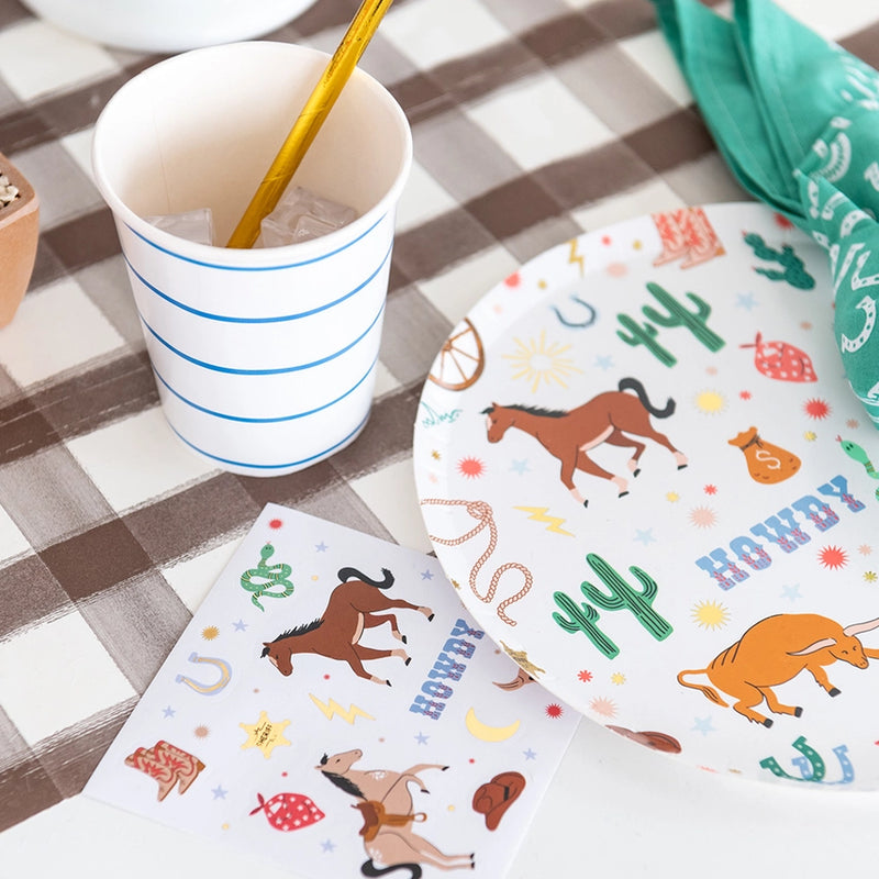 Place setting detail (green napkin): Side angle showing a plate with western icons next to a green bandana napkin and white cup with blue stripes.