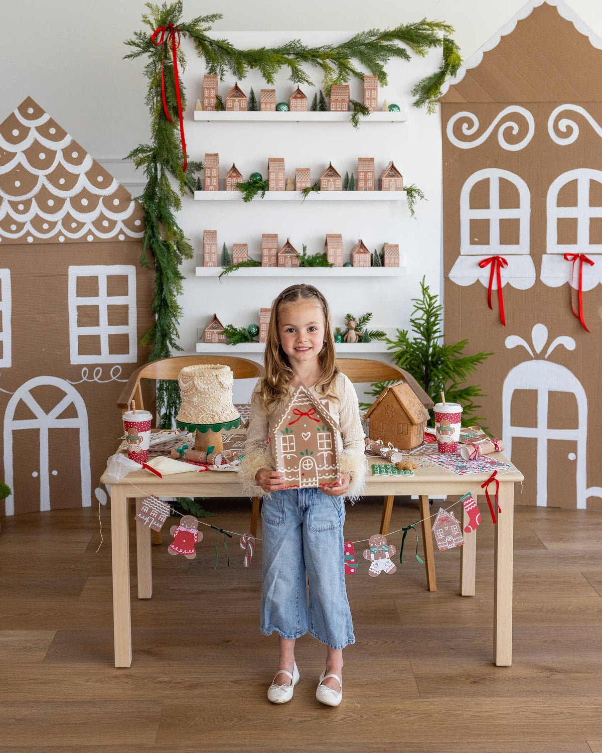 Child standing in a holiday-decorated room holding a Ginger House Plate at a Christmas table.