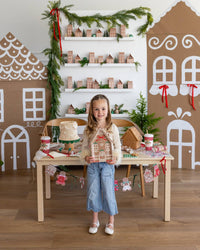 Child standing in a holiday-decorated room holding a Ginger House Plate at a Christmas table.
