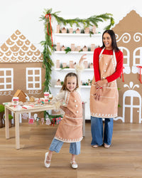 Child posing happily in matching gingerbread apron beside mother during a festive baking scene.
