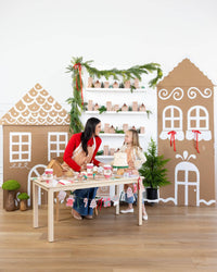 Mother and daughter wearing matching gingerbread aprons while baking together at a gingerbread-themed holiday table.