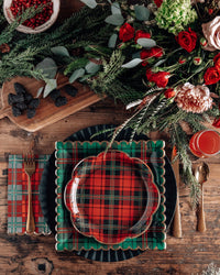 Plaid scalloped plate used in a Christmas place setting with greenery and red drink