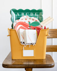 Green alphabet paper plate styled in a yellow school supply bin with apple and notebook plates for a back to school setup
