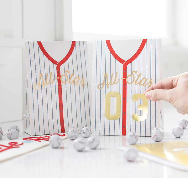 Treat bags designed like baseball jerseys, including sticker numbers for personalization at a kids' baseball party.