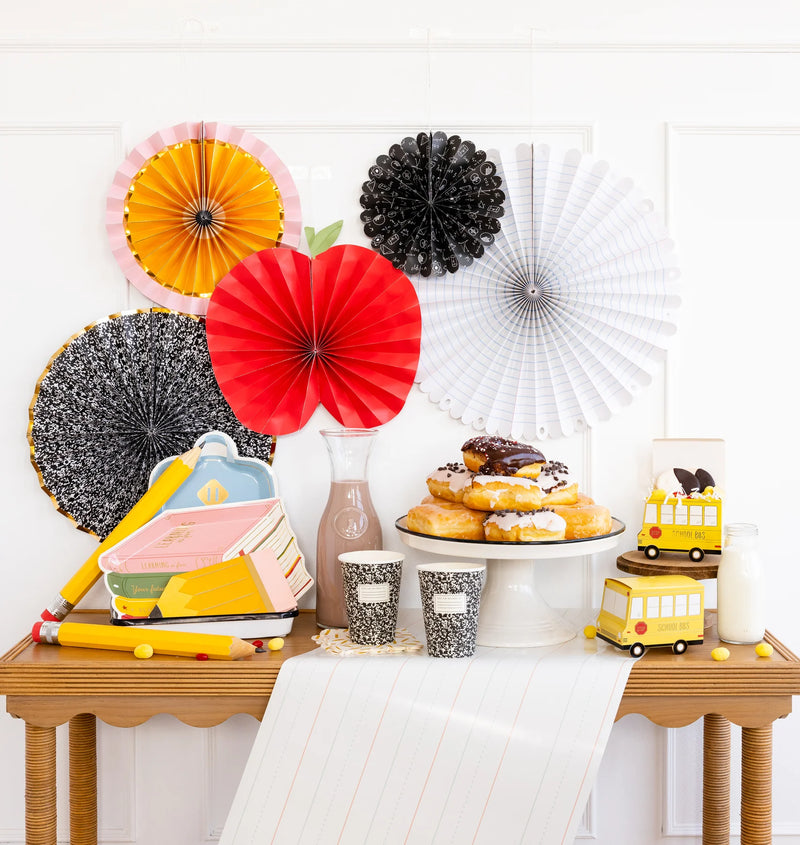 A back-to-school breakfast spread featuring donuts, milk, and chocolate milk on a wooden table, decorated with themed paper fans and school-inspired props.