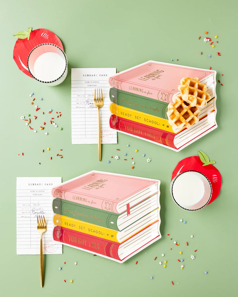 Apple napkins styled with book-shaped plates, milk glasses, gold forks, and library card decor.