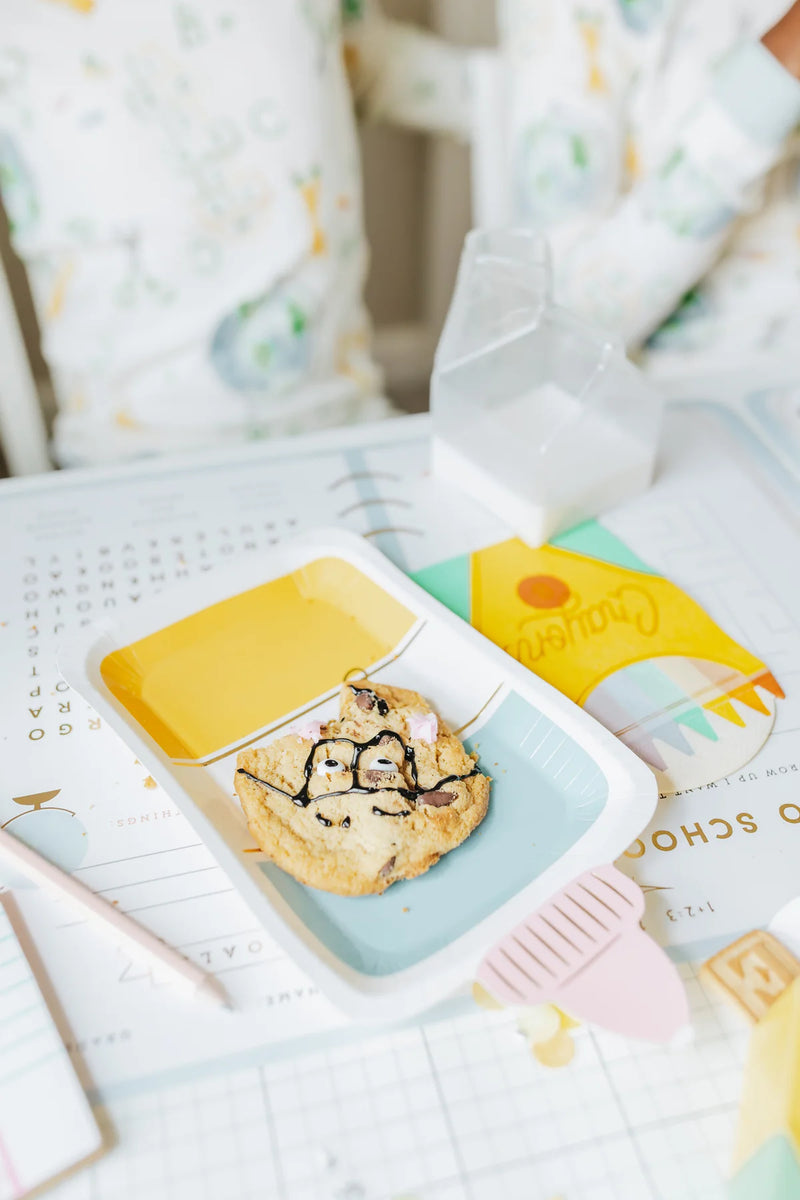 Close-up of cookie decorated with a face on a glue bottle plate, set on a back-to-school placemat.