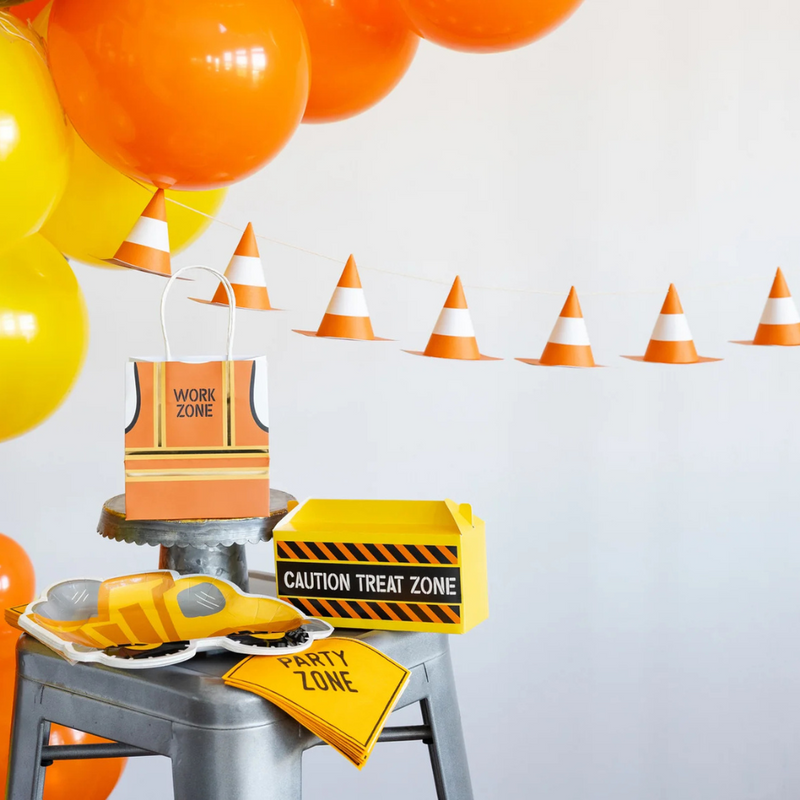 Close-up of banner setup with cones, bags, and treat box under orange/yellow balloons