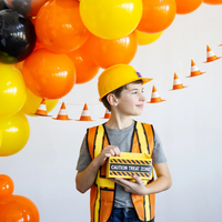 Young boy in a construction costume smiling with cone banner and orange/yellow balloons