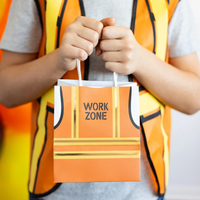 Child holding up "Work Zone" construction vest treat bag with balloons in background