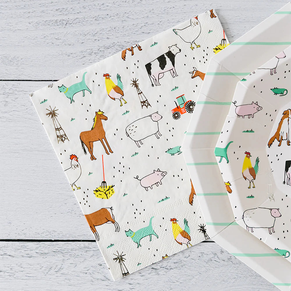 Farm‑print square paper napkin beside octagon plate with matching animal design on white wood background.