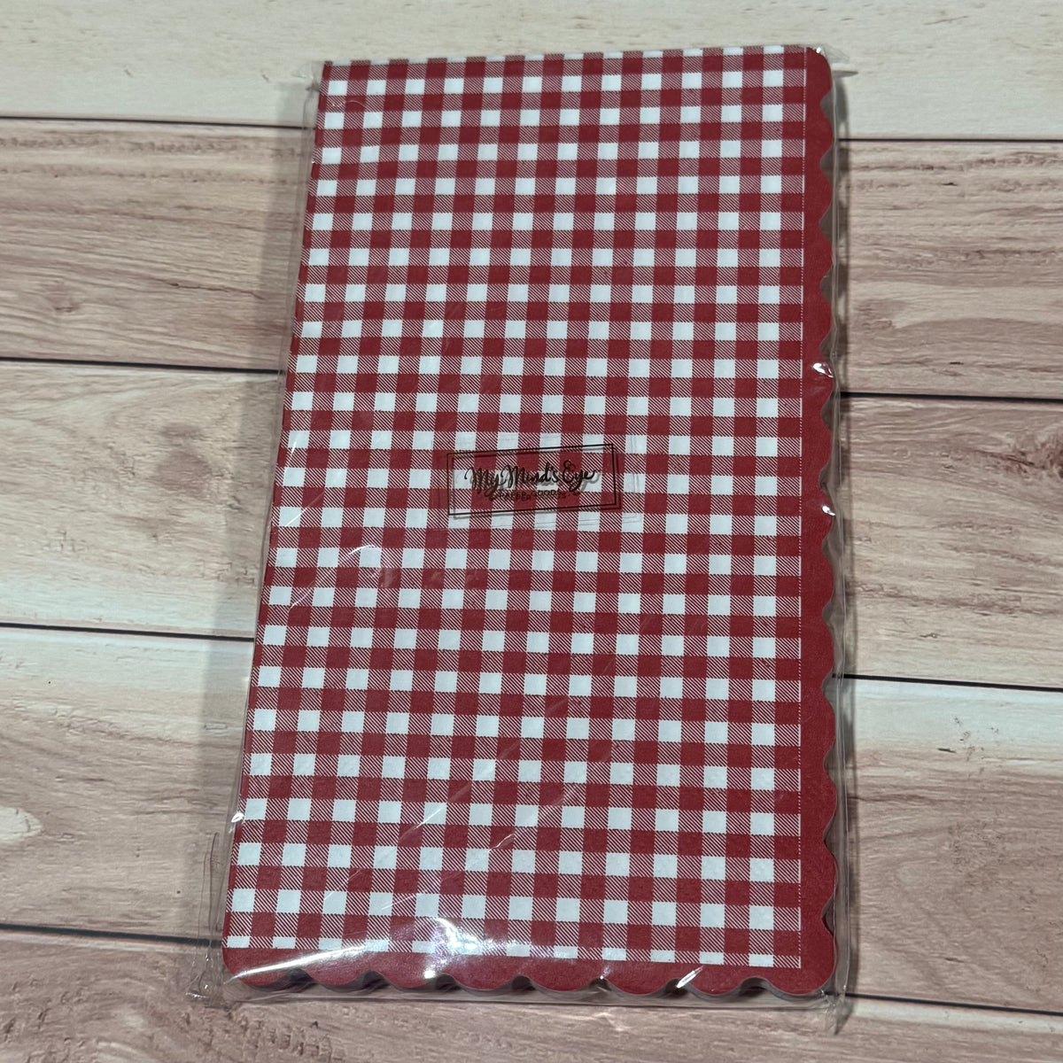 A red and white gingham patterned napkin with scalloped edges, sealed in clear plastic packaging.
