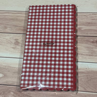 A red and white gingham patterned napkin with scalloped edges, sealed in clear plastic packaging.