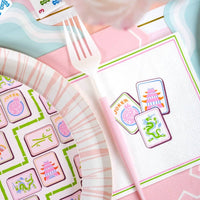 Party supplies including plates, napkins, and a fork with colorful designs on a pink background.