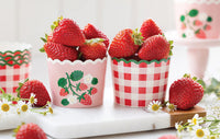 Close-up lifestyle image of two baking cups—one pink with strawberries and one gingham—both filled with juicy strawberries on a white marble countertop.