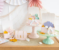 Adorable treasure boxes displayed on a beach-inspired table setting, complete with pastel-colored paper fan decorations and a charming fishing net backdrop.
