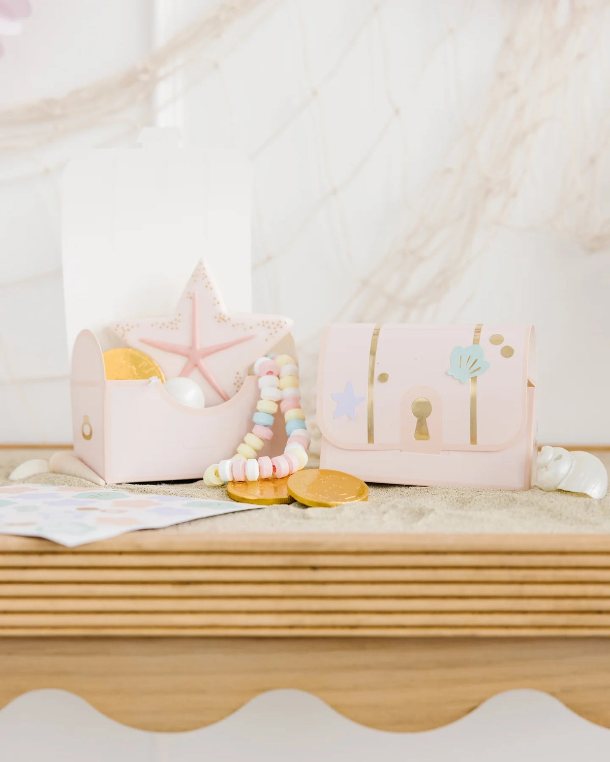 Sweet setup of mermaid treasure treat boxes overflowing with pastel-colored candy necklaces, golden chocolate coins, and intricately decorated mermaid and seashell cookies.