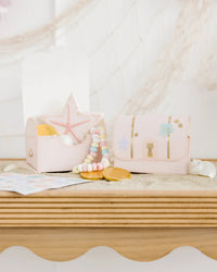 Sweet setup of mermaid treasure treat boxes overflowing with pastel-colored candy necklaces, golden chocolate coins, and intricately decorated mermaid and seashell cookies.