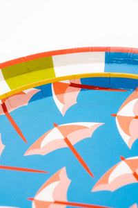 A close-up of colorful dessert plates featuring a vibrant blue background with pink umbrellas and a bright yellow plate with playful beach balls, perfect for a pool party.