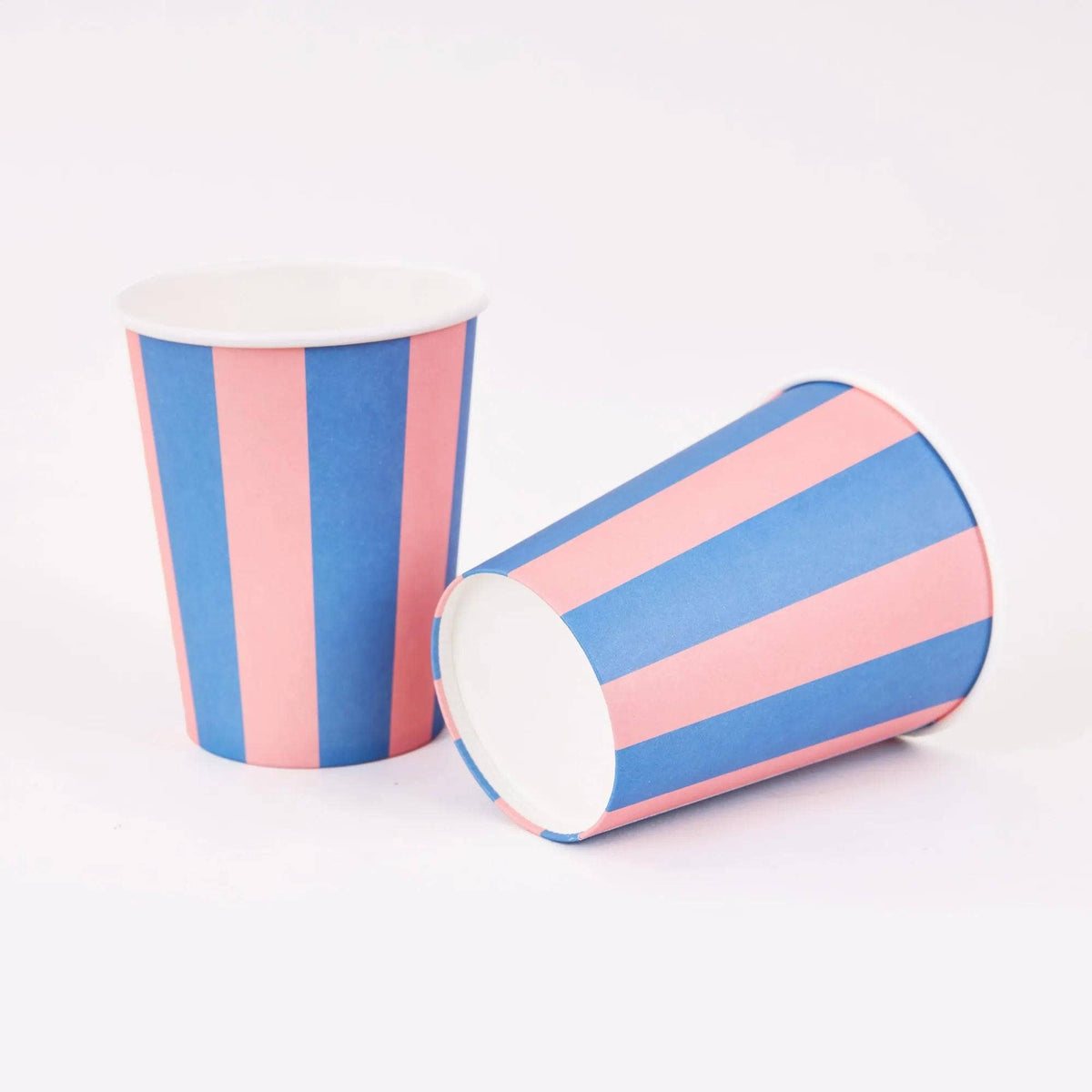 Two pink and blue cabana stripe paper cups, one upright and one on its side, on a white background.