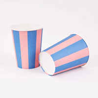 Two pink and blue cabana stripe paper cups, one upright and one on its side, on a white background.