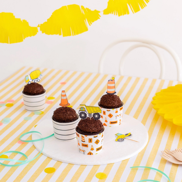 Cupcakes displayed on a yellow-striped table, topped with dump truck and cone toppers.