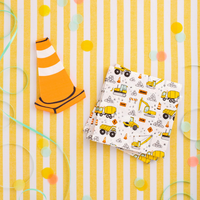Construction-themed party table with yellow striped tablecloth, traffic cone-shaped napkin, and folded large napkins covered in illustrated construction vehicles and signs.