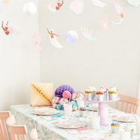 Mermaid and seashell die-cuts strung as a banner above a party dessert table with pastel cupcakes.