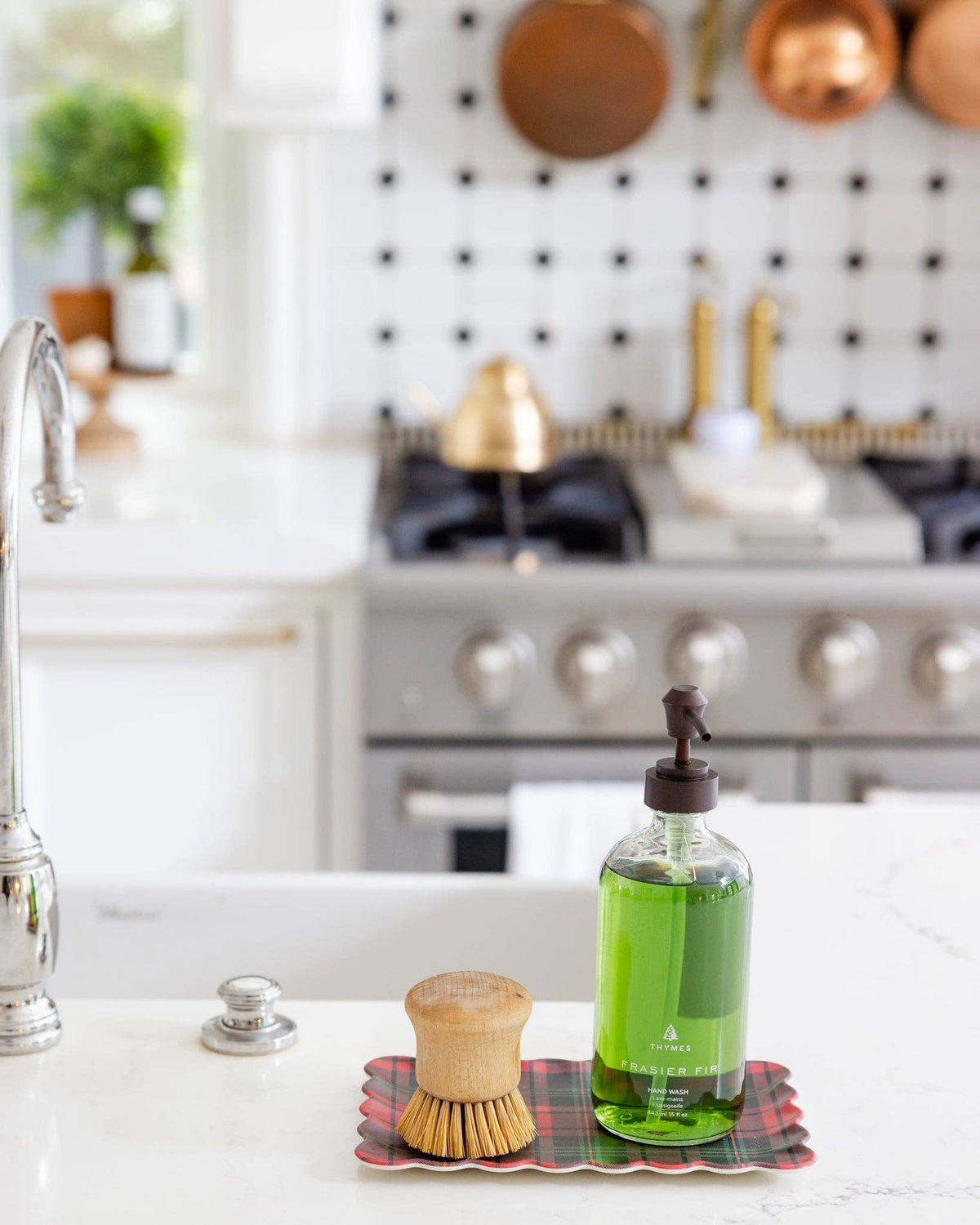 Plaid bamboo tray holding soap brush and green hand soap bottle on a kitchen counter