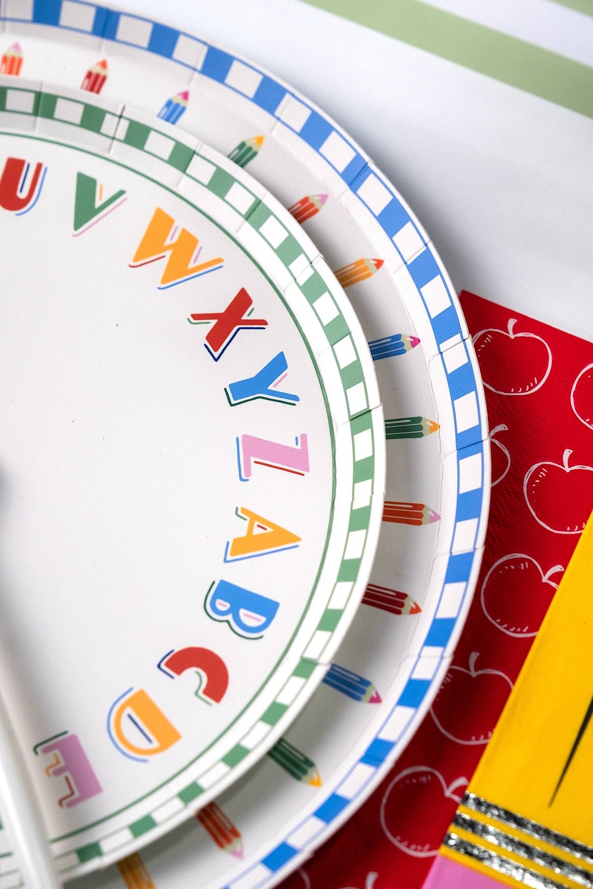 Close-up of alphabet paper plate and pencil-rim paper plate edges on a red apple-print paper runner