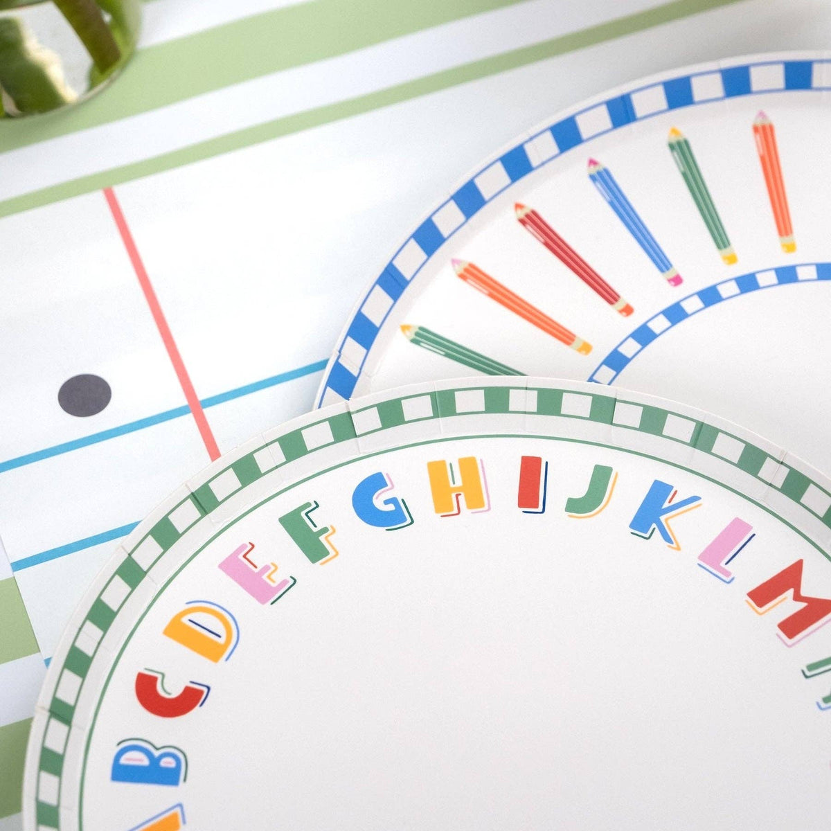 Close-up of alphabet paper plate and pencil-rim paper plate showing the green checkered border, multi-color alphabet letters, and colored pencil illustrations
