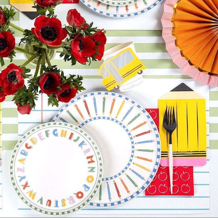 Single back-to-school place setting featuring the ABC alphabet plate layered under a pencil-rim plate, with a yellow pencil-shaped napkin, school bus napkin, and red anemones in a glass vase