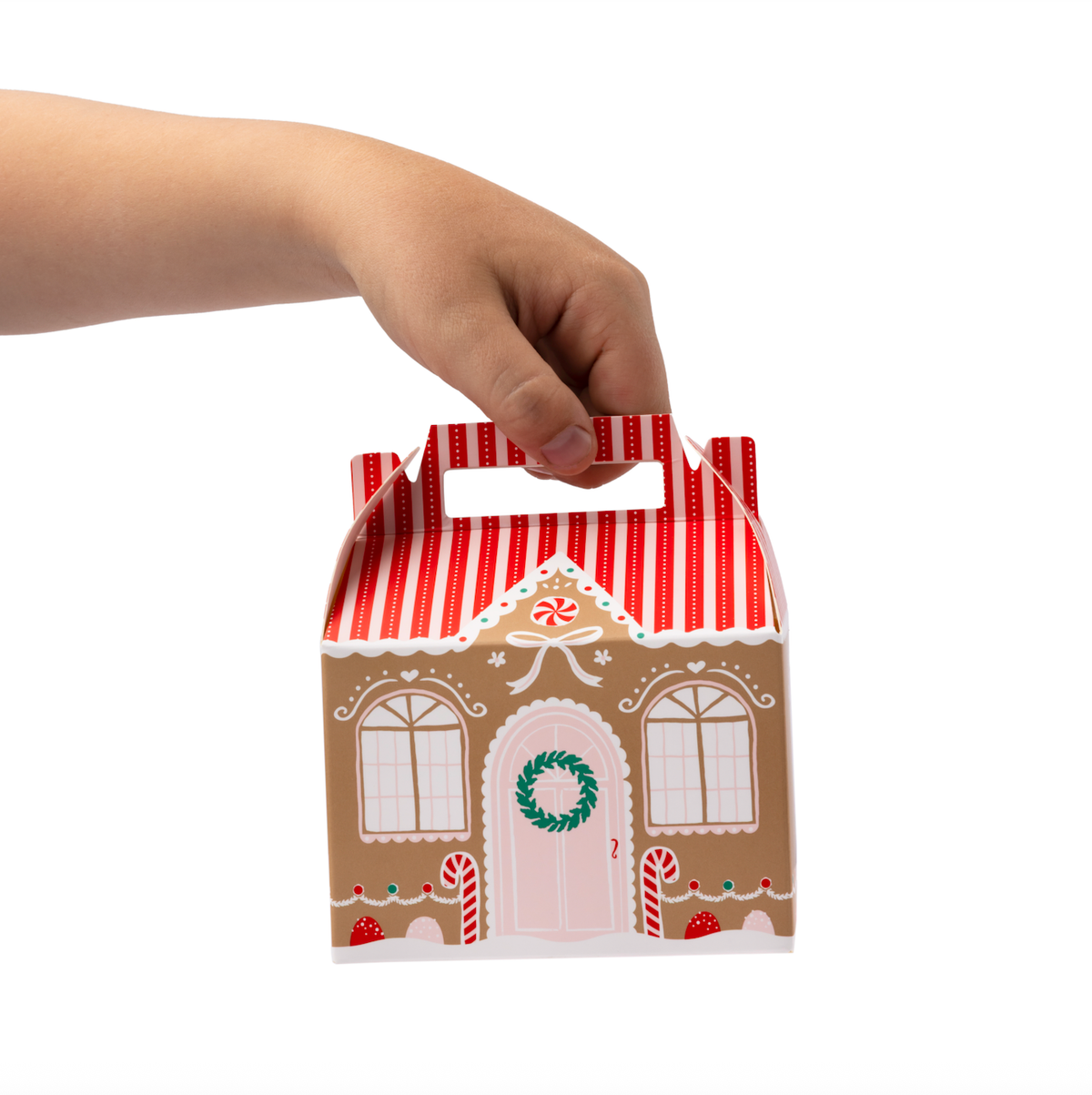 Hand holding assembled gingerbread house treat box with striped roof and candy details.