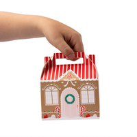 Hand holding assembled gingerbread house treat box with striped roof and candy details.
