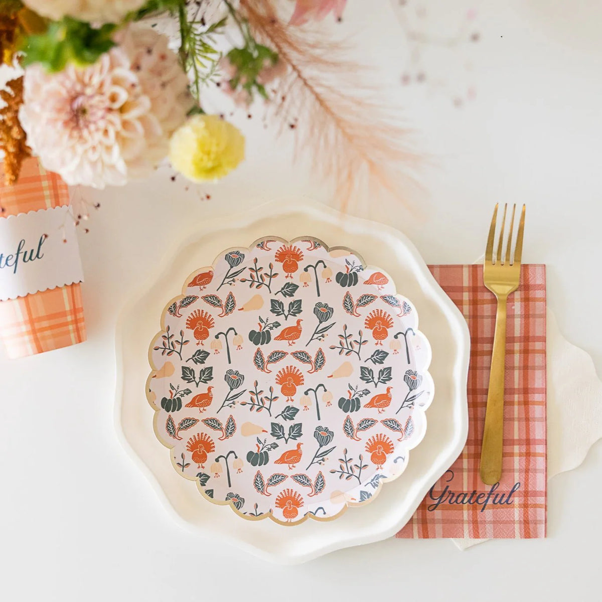 Single place setting with patterned dessert plate and gold fork on plaid napkin.
