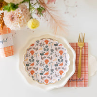 Single place setting with patterned dessert plate and gold fork on plaid napkin.