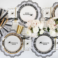 An overhead view of a graduation tablescape with Congrats Grad plates, gold cups, and white peonies.