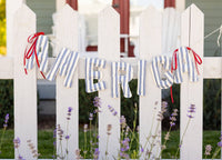 Blue and cream striped America banner hung across white picket fence with lavender below
