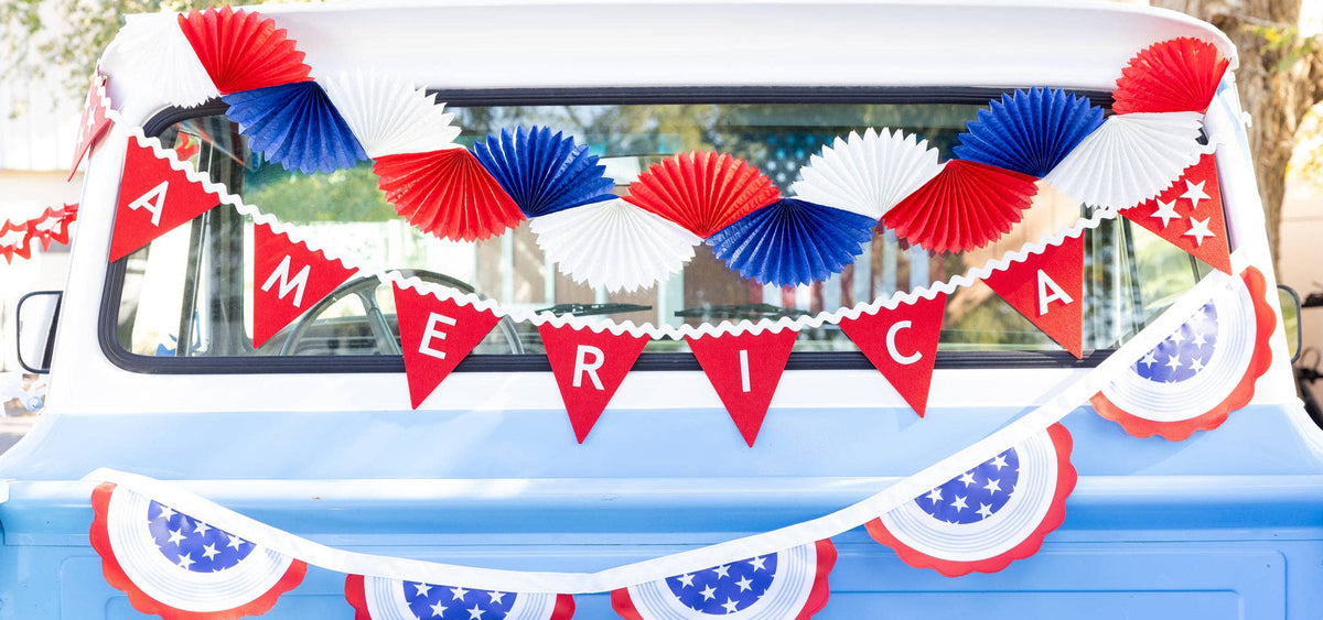 Close-up of America red felt pennant banner letters and star accents with red white and blue paper fan garland