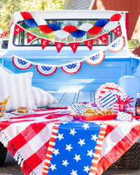 Close-up of vintage truck bed styled as a 4th of July picnic with America felt pennant banner, paper fan garland, bunting, and summer food
