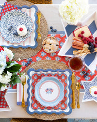 Hamptons Americana full tablescape overhead with American flag scalloped plates, blue ditsy floral plates, red striped dinner plates, red block-print napkins, star trays, hydrangeas, and gold cutlery
