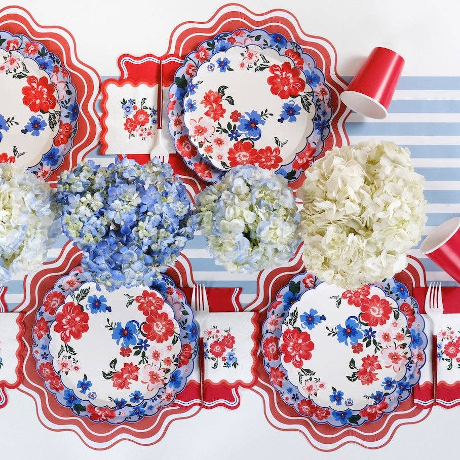 High-end Americana garden party table featuring blue striped linens, floral plates, and red scalloped napkins.