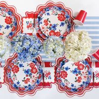 High-end Americana garden party table featuring blue striped linens, floral plates, and red scalloped napkins.