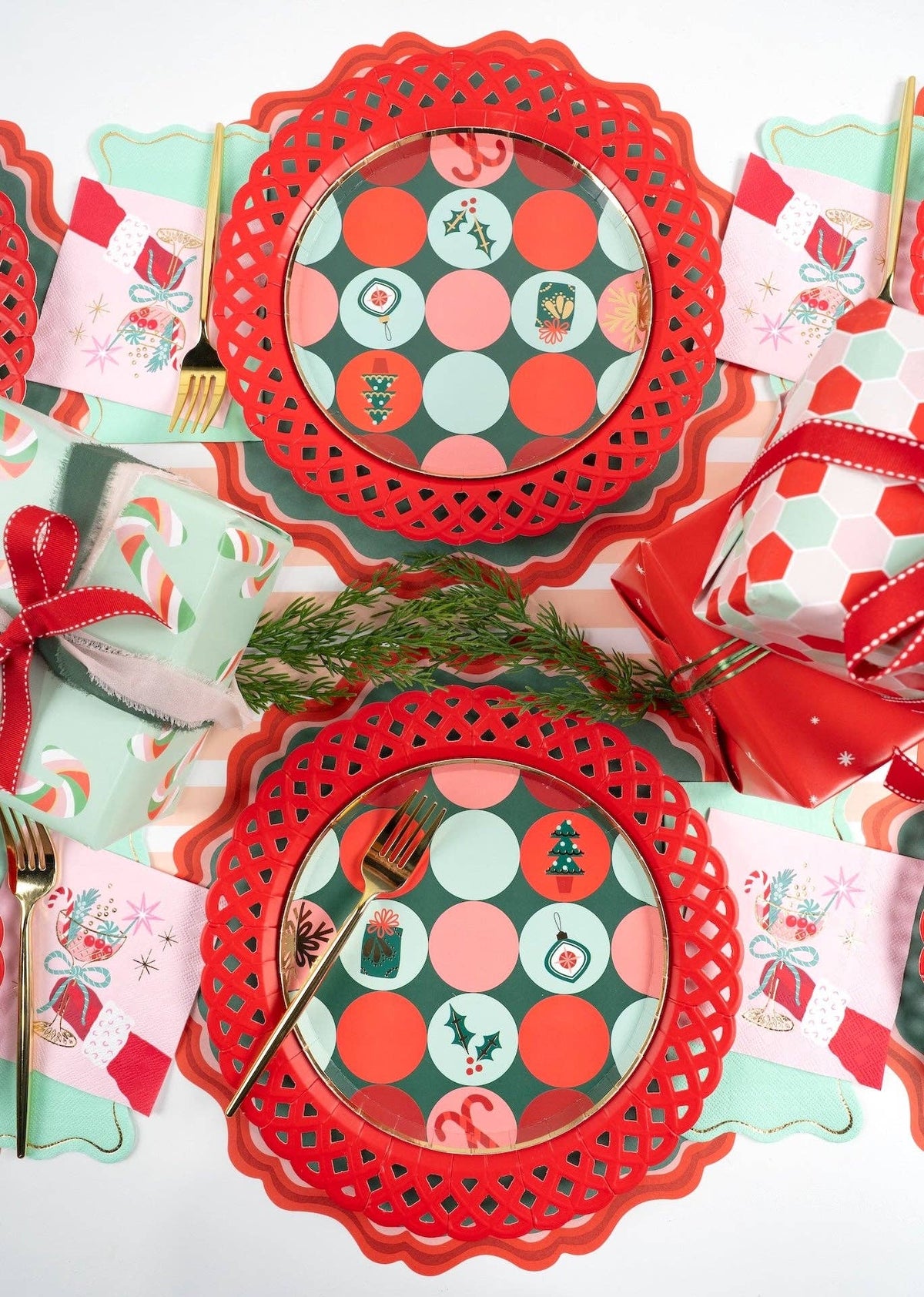 Close-up angled shot of multiple place settings featuring red scalloped chargers layered with retro green and red dot paper plates.