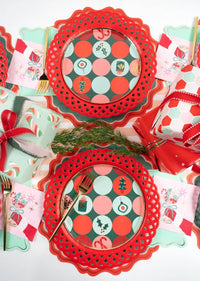 Close-up angled shot of multiple place settings featuring red scalloped chargers layered with retro green and red dot paper plates.