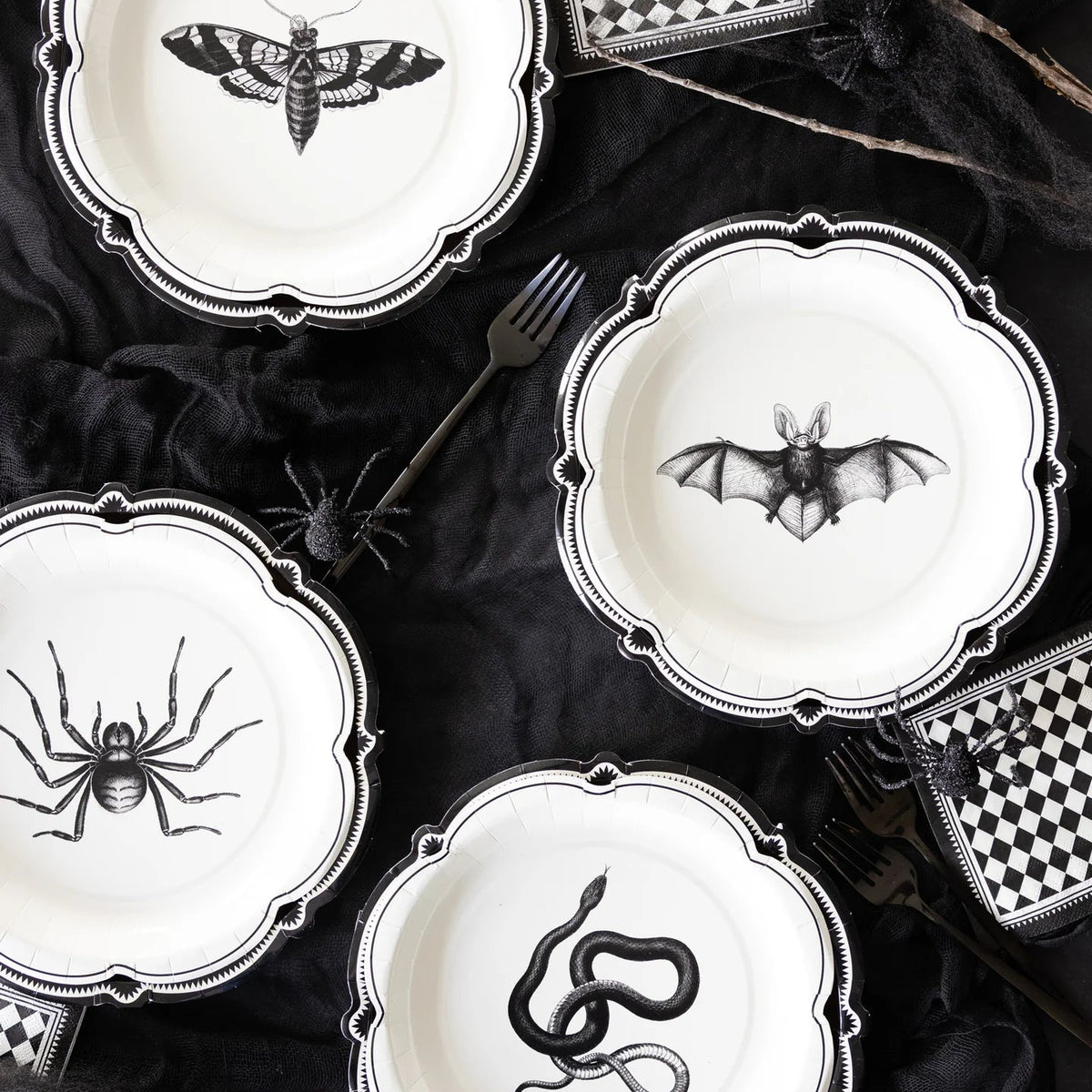 Halloween-themed plates with black spider, bat, and snake designs on a dark surface.