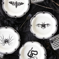 Halloween-themed plates with black spider, bat, and snake designs on a dark surface.