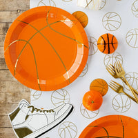 Orange ball plates and gold forks with sneaker napkin—stylish basketball party supplies.