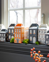 Close-up of assembled halloween treat boxes—mini house designs in orange, black, gray, and cream—styled on a rainy-day windowsill with moss accents.