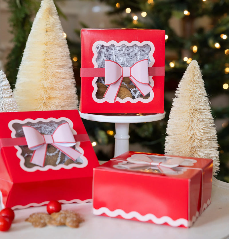 Three assembled red Christmas cookie boxes with pink 3D bows, displayed around a white bottlebrush tree.